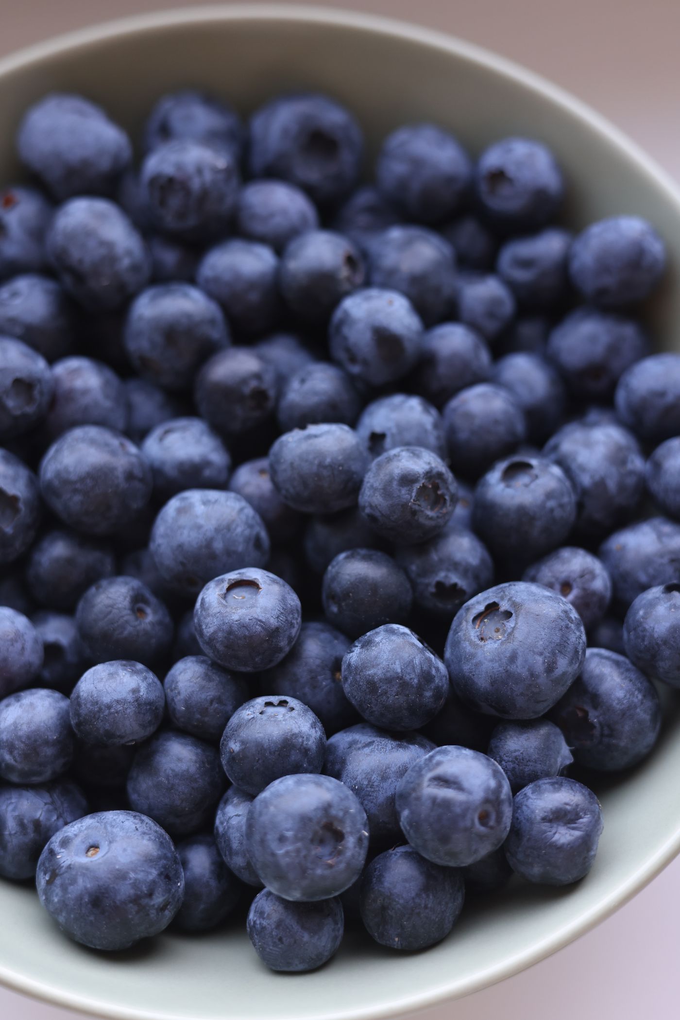 A wooden bowl of fresh blueberries showing the silvery bloom on their skins